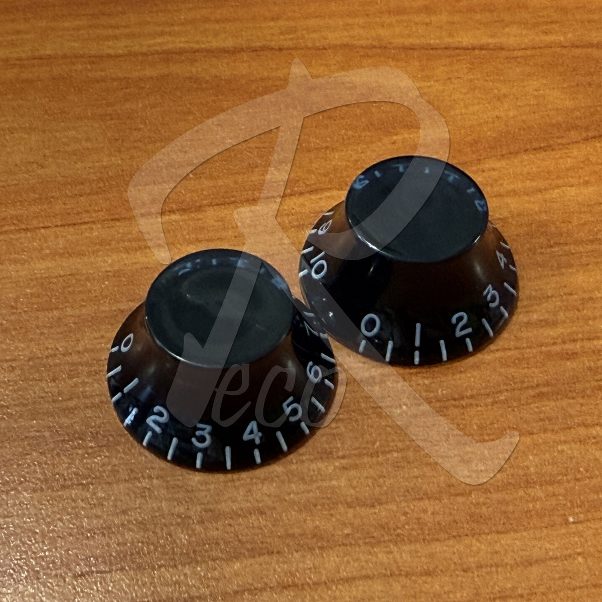 Two black guitar knobs with number labels on a wooden surface