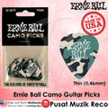 Ernie Ball camo guitar picks shown both in retail packaging and as a single pick. The product features a green, beige, and black camouflage pattern with 'Ernie Ball' printed in white.