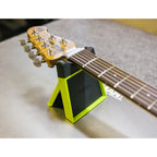 A guitar headstock and neck resting on a black and neon yellow guitar stand on a gray table.