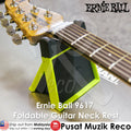 Ernie Ball 9617 foldable guitar neck rest in black and neon yellow-green, shown supporting a guitar neck on a gray surface. The Ernie Ball logo is visible on the headstock, and product text overlays appear around the image.