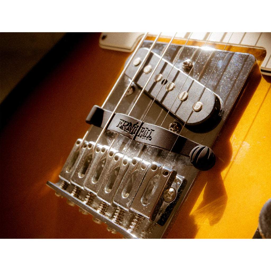 Close-up of a tremolo bridge on an electric guitar, showing the black tremolo bar, silver metal hardware, and part of the sunburst orange guitar body.