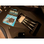 Ernie Ball spring damper set for a guitar tremolo system, shown with its original retail packaging next to the hardware installed on a black guitar body.