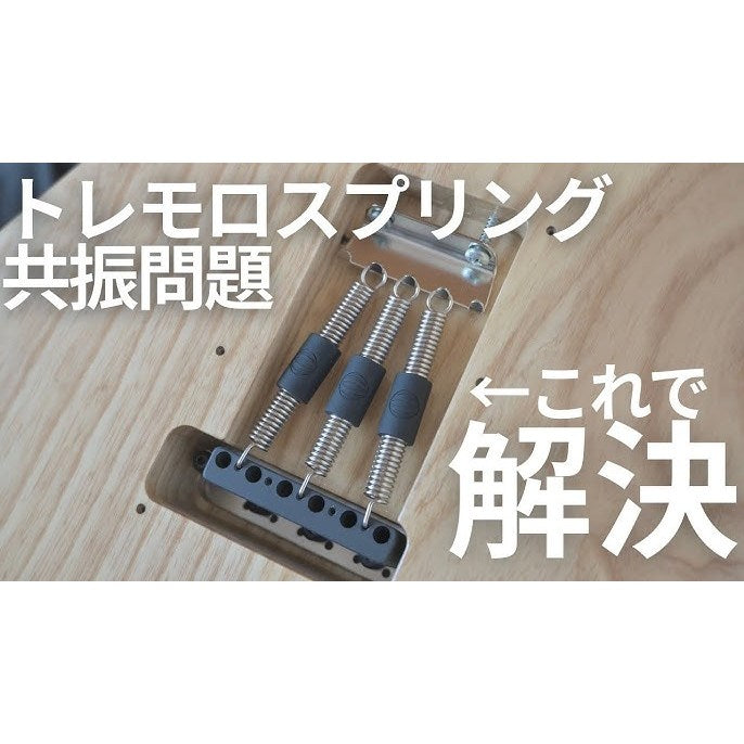 Close-up of a guitar tremolo bridge with three metal springs and dark gray rubber dampeners, shown on a light wood surface with large Japanese text overlaid.