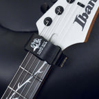A close-up of a black guitar headstock strap by Devoted-Tools holding an Ibanez bass guitar neck. The strap features a white graphic of a tree with branches and the text 'DEVOTED-TOOLS' and 'ignition'.