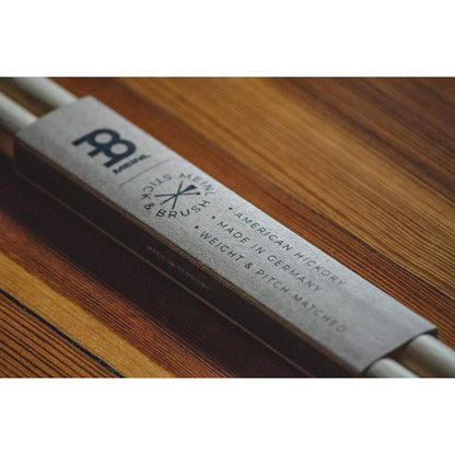 A close-up of a Meinl US 124 double bass reed mouthpiece wrapped in a gray paper sleeve, resting on a wooden surface.