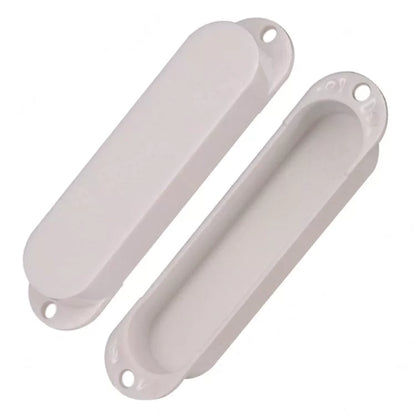 Two white plastic guitar bridge covers, one showing the smooth outer shell and the other showing the inner channel, on a plain white background.
