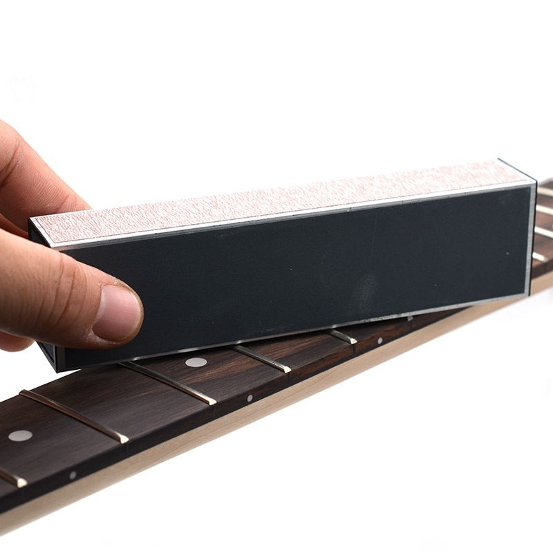 A hand holds a rectangular black guitar string winder against a dark wood fretboard, shown on a clean white background.