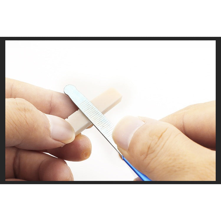 A close-up of hands using a small metal nail file to smooth a beige nail tip against a white background.