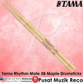 A pair of Tama Rhythm Mate 5B maple drumsticks shown diagonally on a pink textured background with Tama branding and product text overlays.
